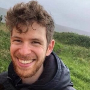 Outdoor headshot of a smiling man on a green hillside