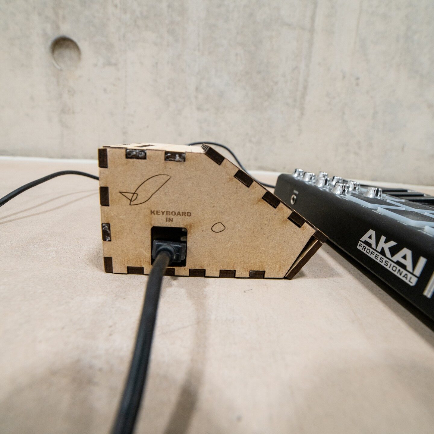 Rear of the laser-cut coach box engraved 'Keyboard in', cable plugged in, Akai keyboard beside it