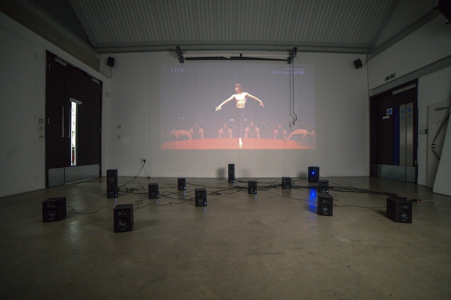 Dark wide view of fifteen floor speakers before a projection of Guillem dancing Bolero