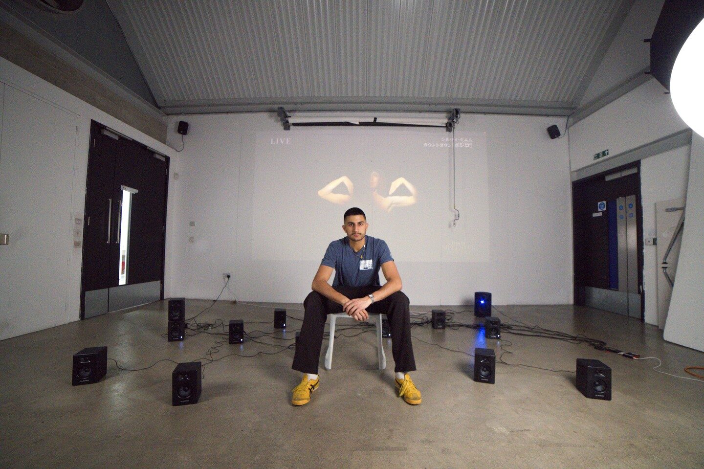 Artist seated centre of the speaker ring, projected dancer's arms framing his head