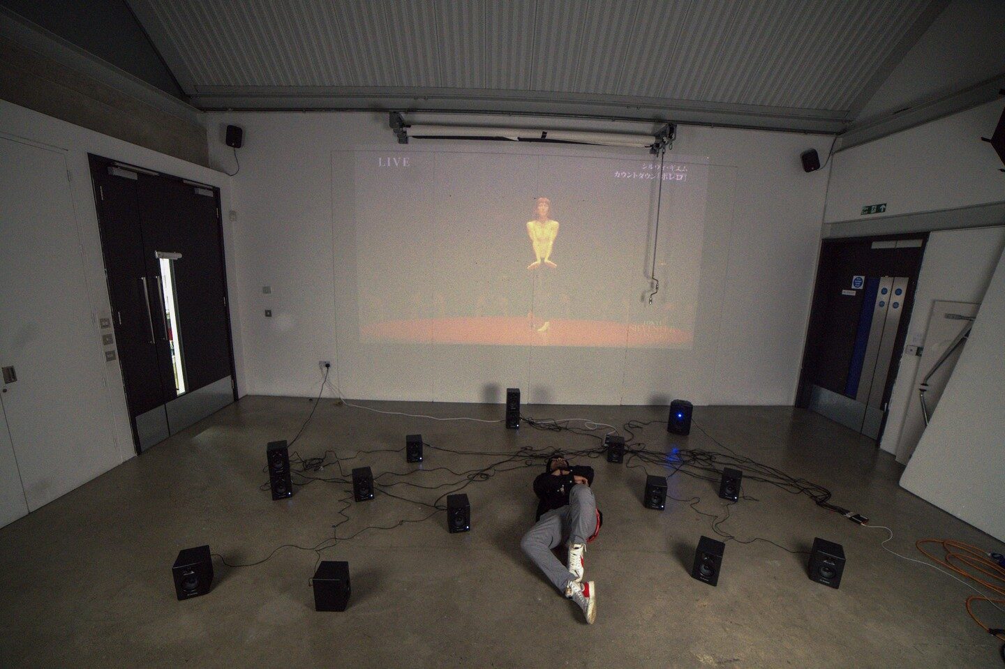 Person lying flat among the floor speakers beneath the projected Bolero dancer
