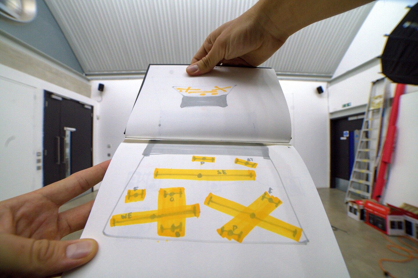 Sketchbook of yellow marker speaker-layout plans held open inside the studio