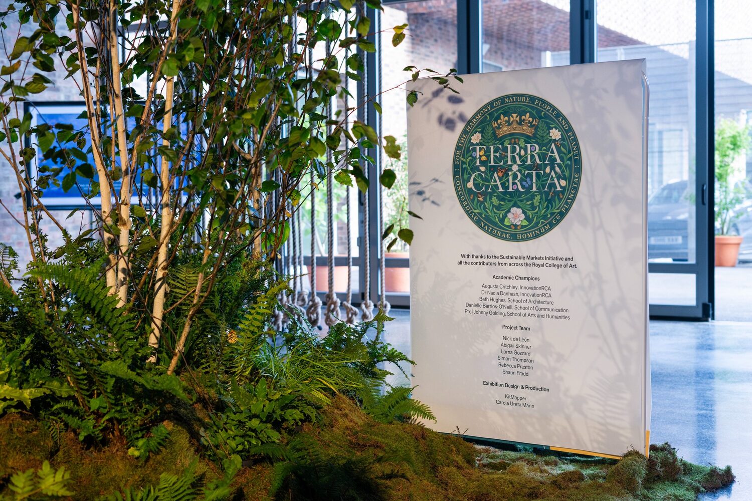 Terra Carta credits board surrounded by ferns and moss at the exhibition