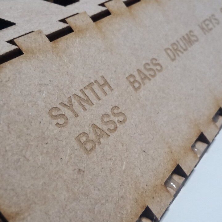 Square macro of engraved SYNTH BASS, BASS, DRUMS, KEYS labels on the MDF wedge